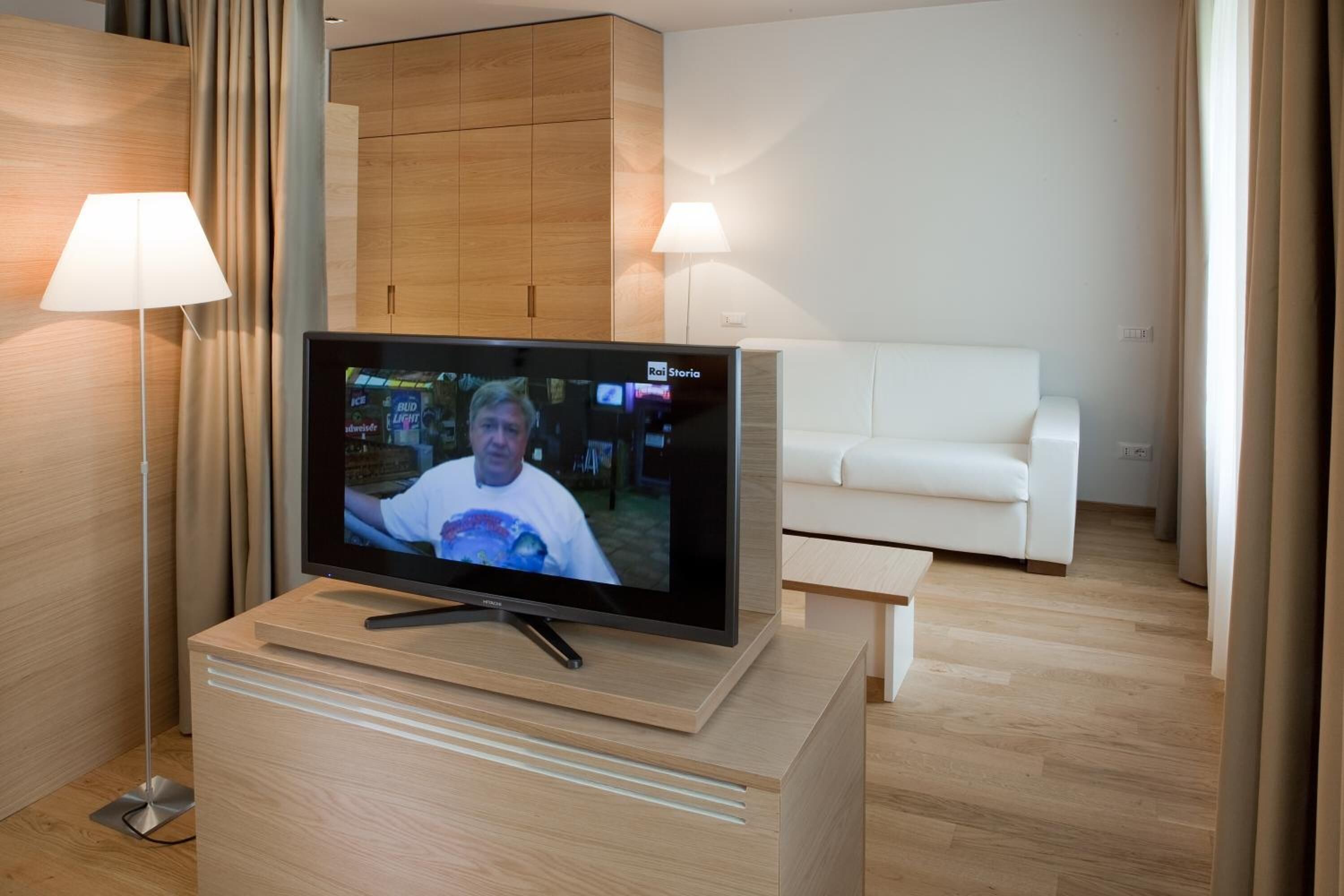A modern living room with a flat-screen TV on a wooden stand, a white sofa, and a lamp.
