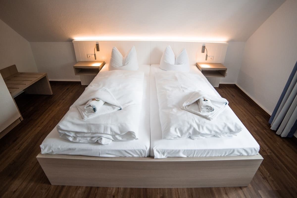 A double bed with white linens, two bedside tables, and a wooden floor.