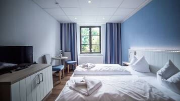 Ein Hotelzimmer mit zwei Betten, einem Fernseher, einem Schreibtisch und einem fensterbepflanzten Fenster.