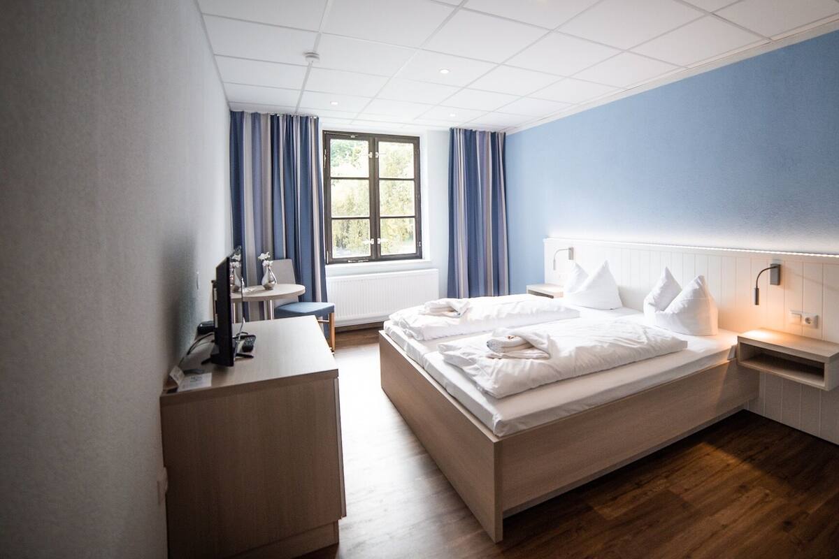 A modern hotel room with a large bed, bedside tables, a desk, and a window with curtains.