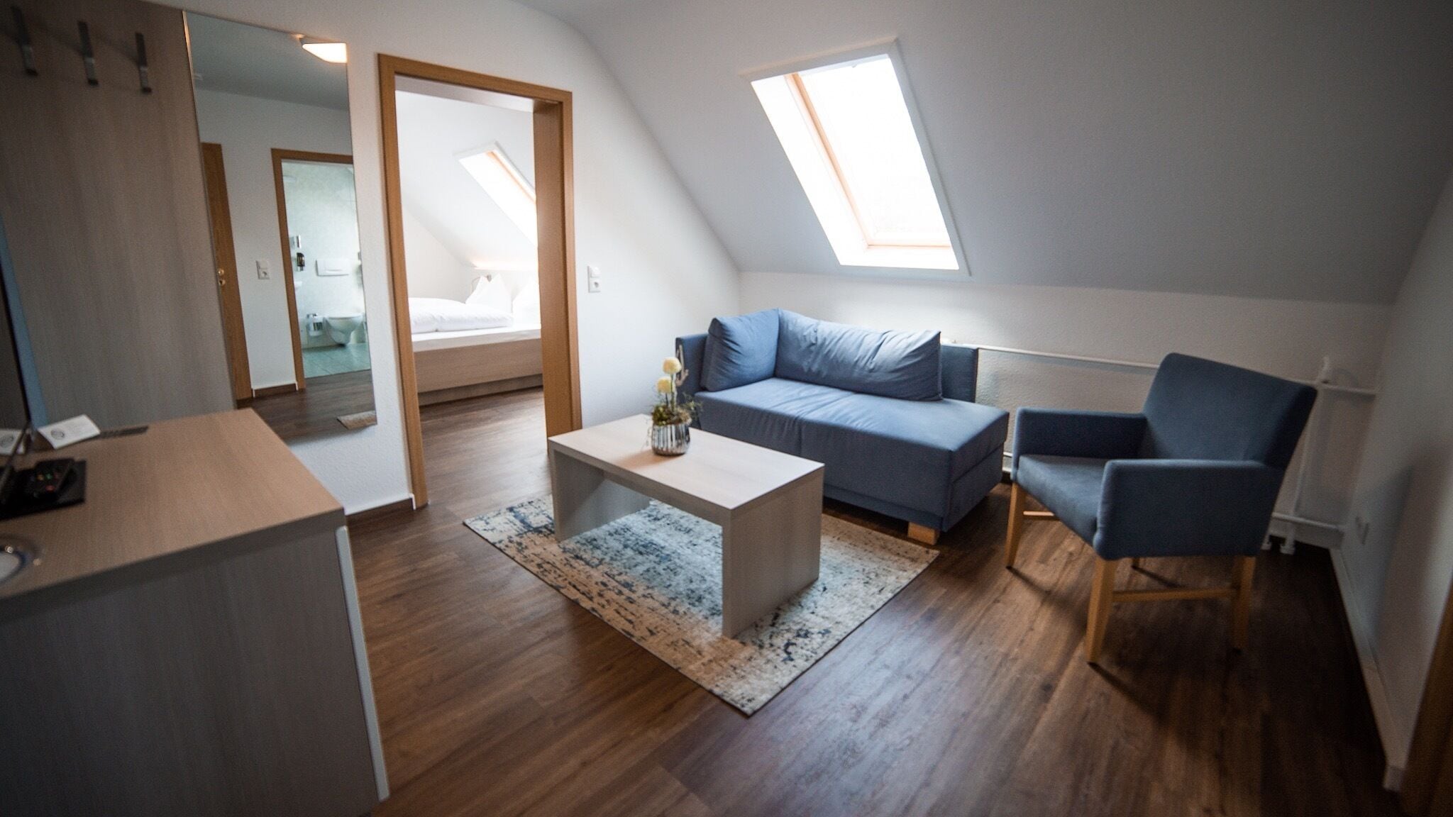Un loft moderno con techo inclinado, un sofá, una silla, una mesita de centro y un escritorio pequeño.