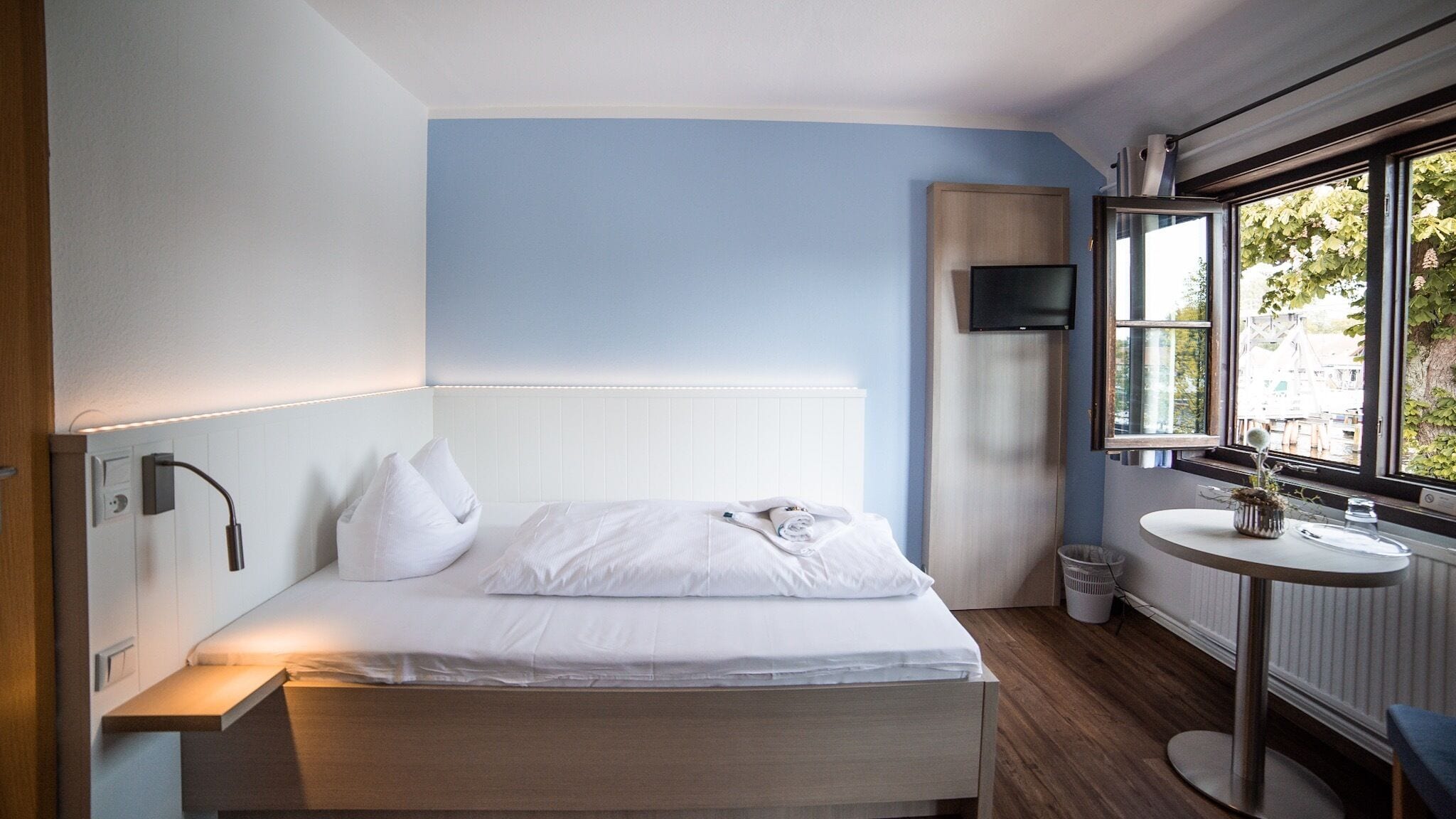 Una camera d'albergo moderna con un letto, un comodino, una TV e una finestra vista esterna.