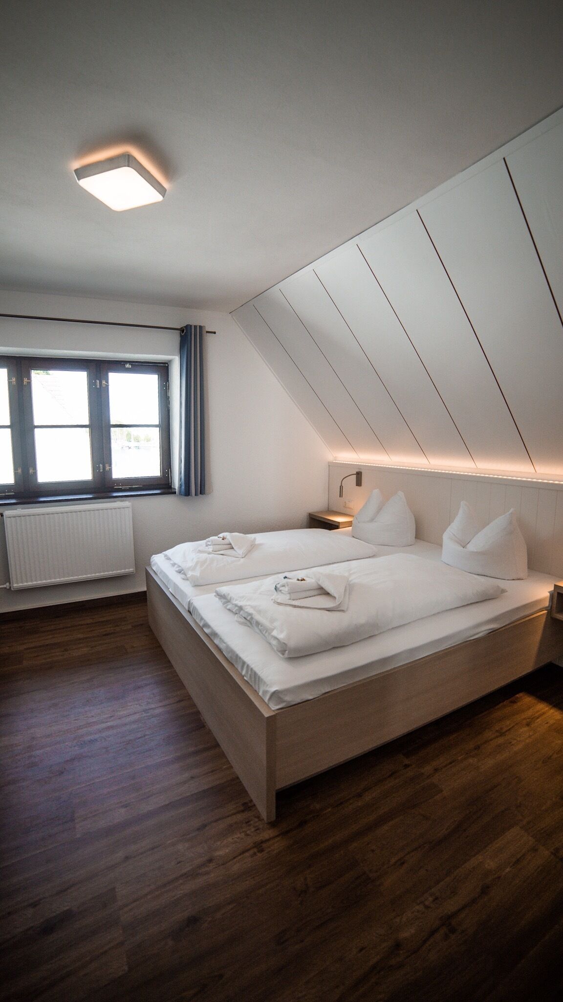 Um quarto moderno com uma cama grande, uma janela com cortinas, um radiador e um teto inclinado.