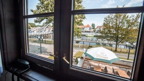 A view through a window with a view of a riverside area, including a bridge, boats, and buildings. - Hotel zur Fähre (Greifswald)