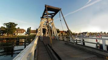 Un puente peatonal de madera sobre el agua, con estructura metálica, que conduce a un puerto deportivo con barcos.