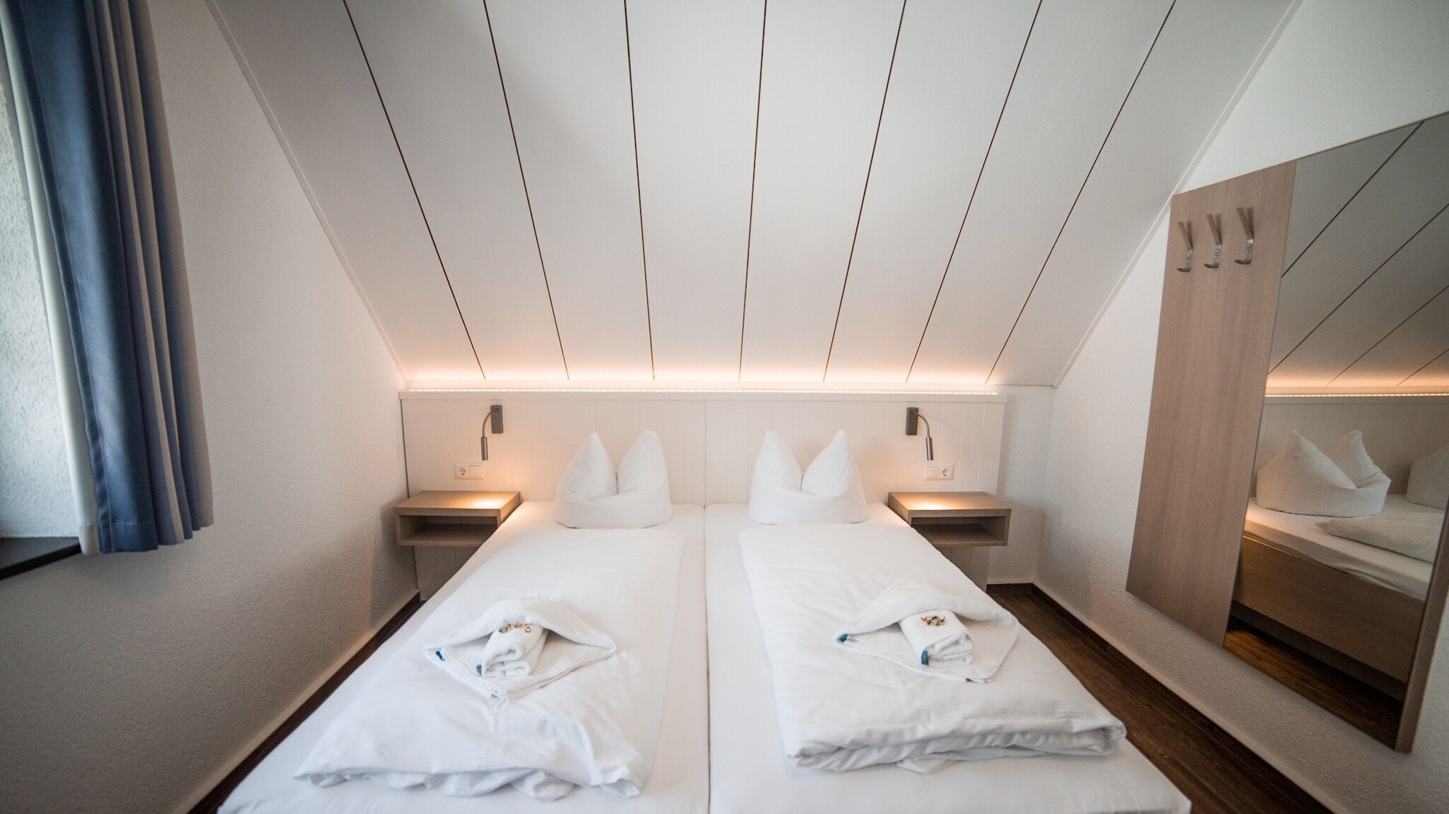A hotel room with two beds, a large mirror, and a wooden wardrobe.