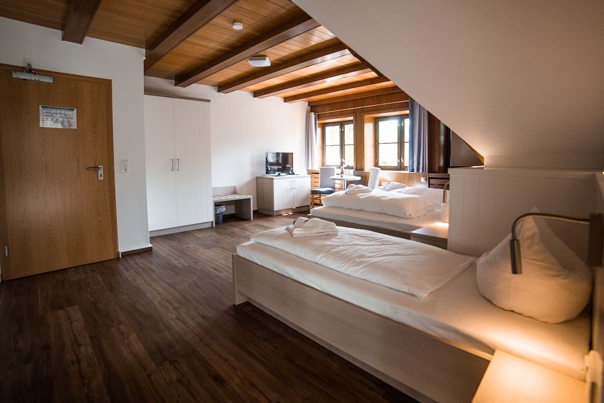 A bedroom with two beds, wooden flooring, and a sloped ceiling with exposed beams.