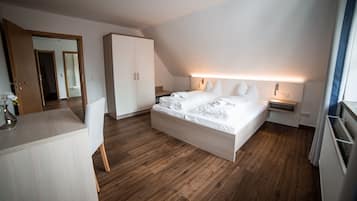 Moderni hotellihuone, jossa on suuri sänky, puulattia, vaatekaappi ja työpöytä, jonka päällä on maljakko täynnä kukkia.