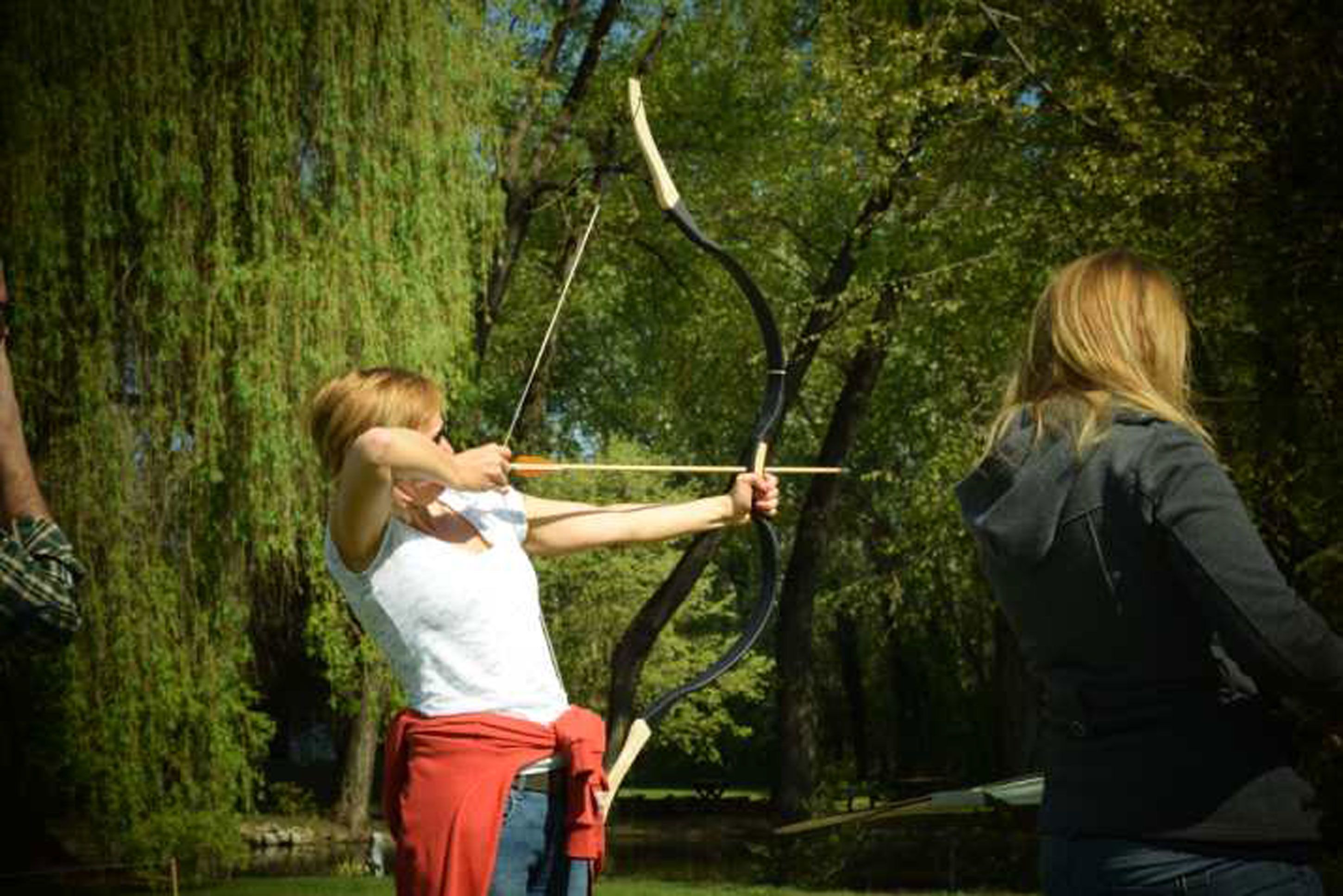 A person aiming a bow in an outdoor setting with trees.