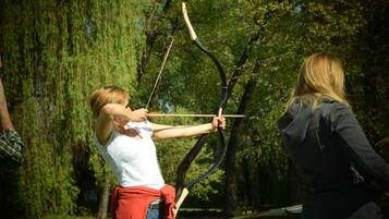 A person aiming a bow in an outdoor setting with trees.