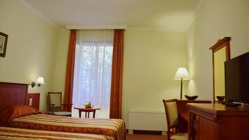 Hotelkamer met twee bedden, een bureau, een stoel, een lamp, een televisie en een raam met gordijnen.