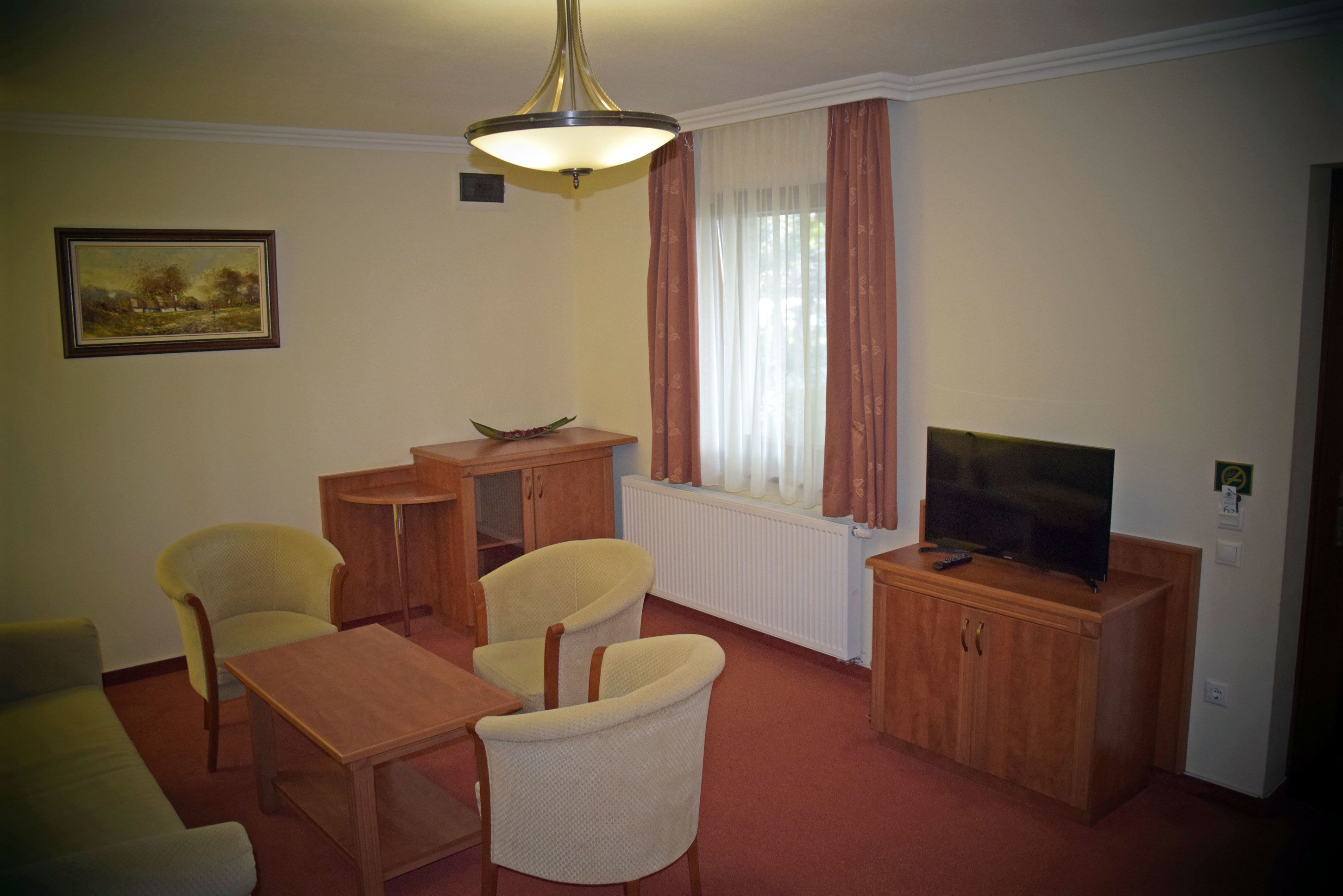 A furnished living room with a sofa, two armchairs, a coffee table, a television, and a radiator.