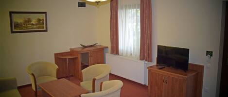 A furnished living room with a sofa, two armchairs, a coffee table, a television, and a radiator.