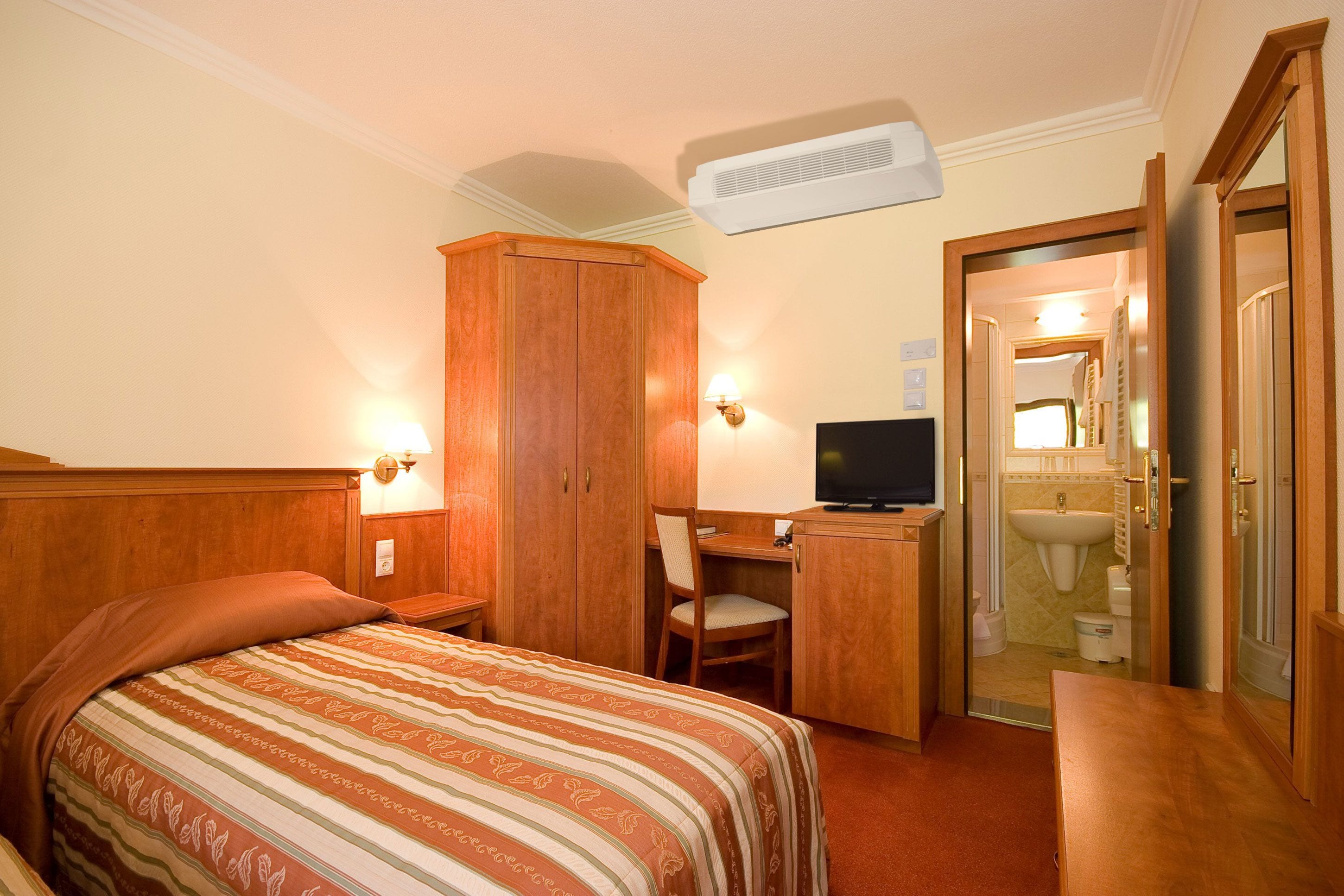 A hotel room with a bed, a desk, a television, and a bathroom visible through an open door.