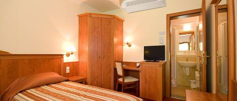 A hotel room with a bed, a desk, a television, and a bathroom visible through an open door.