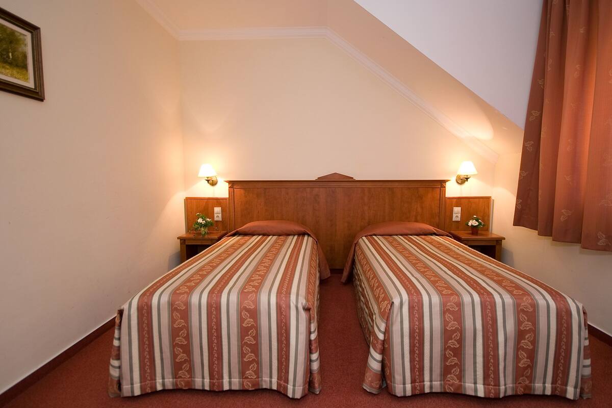 Une chambre avec deux lits simples, chacun doté d’une tête de lit en bois et de lampes de chevet.