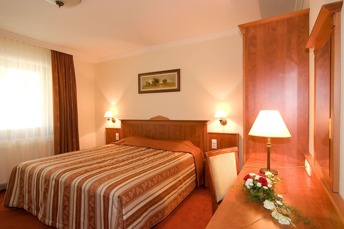 Une chambre d’hôtel avec un grand lit, deux lampes de chevet, une tête de lit en bois, un tableau encadré au mur et un arrangement floral sur la table de chevet.