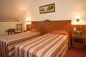 A hotel room with two beds, wooden headboard, bedside lamps, a small table with a chair, and a framed picture on the wall. - Geréby Kúria Hotel és Lovasudvar (Lajosmizse)
