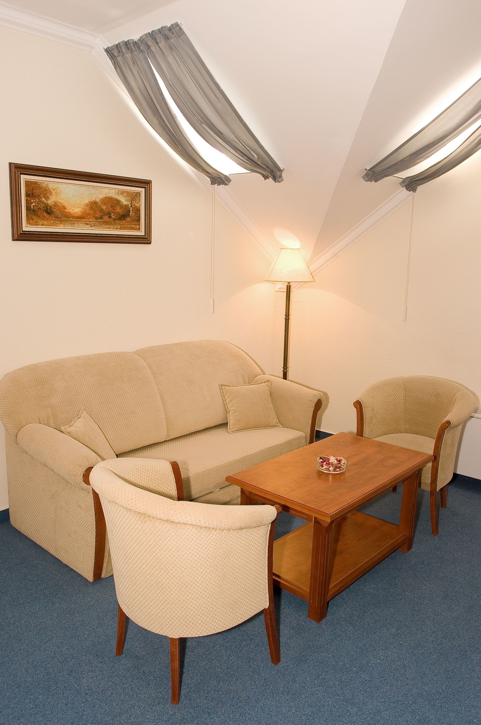 A room with a beige sofa, two armchairs, a wooden coffee table, a floor lamp, and a painting on the wall.