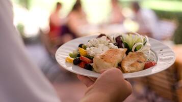 Una persona sosteniendo un plato con comida, que incluye pescado, verduras y arroz, al aire libre.