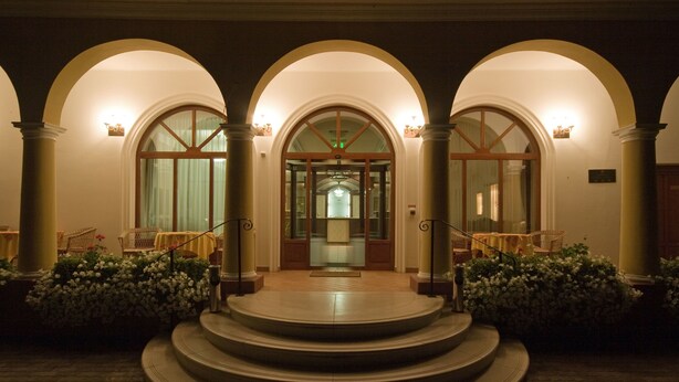 A grand entrance with three arched doorways, a central staircase, and a well-lit interior visible through the doors.