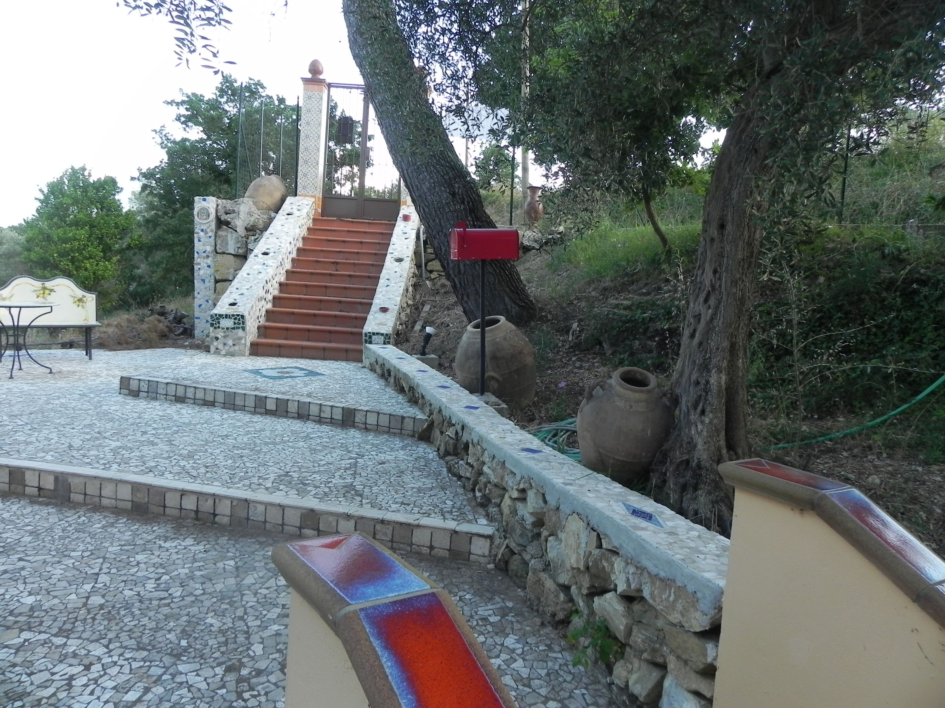 A stone staircase leading up to a building, surrounded by trees and outdoor furniture.