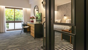 Habitación de hotel con cama, escritorio con computadora, silla, ventana con cortinas y vista a zonas verdes.