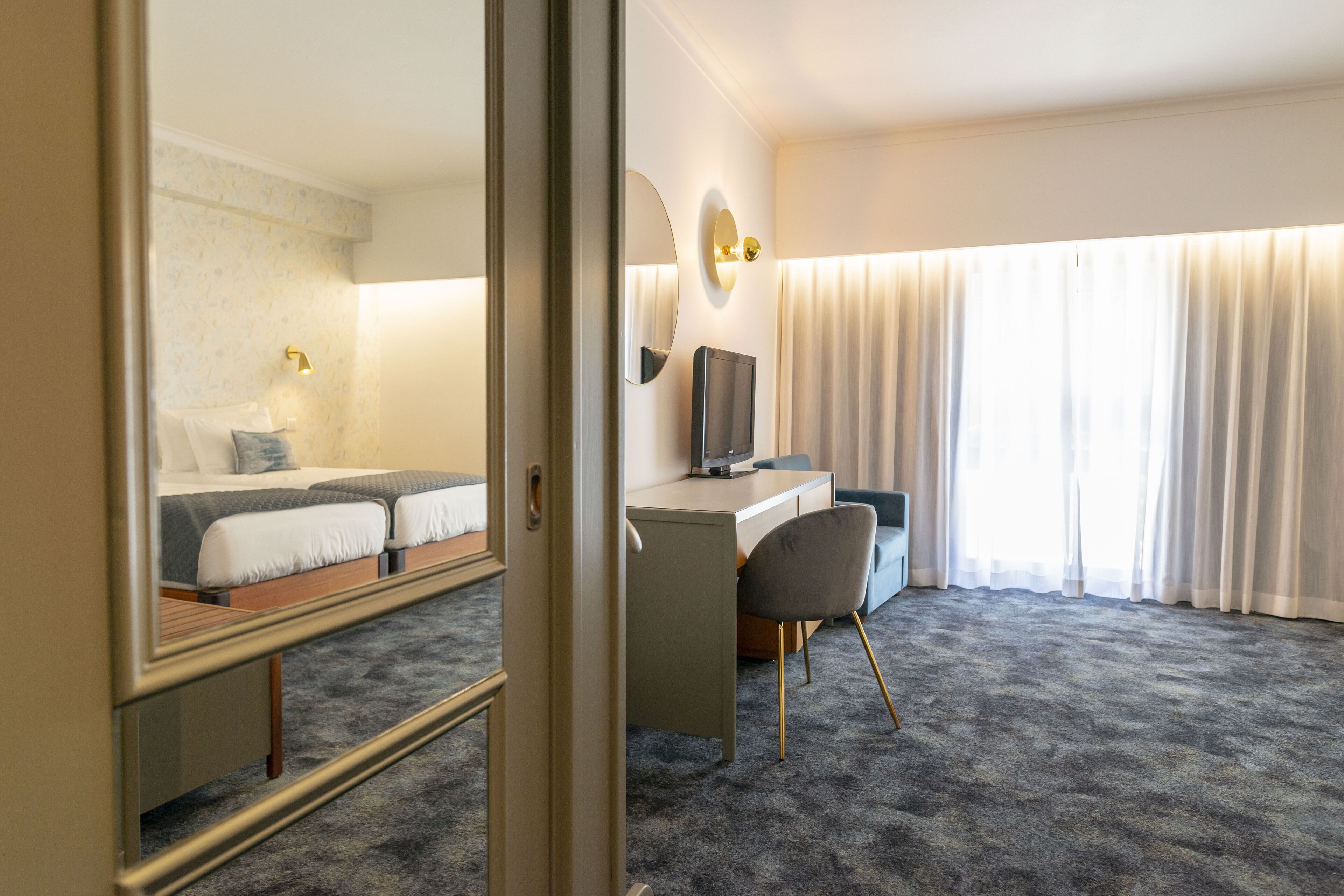 Ein Hotelzimmer mit Bett, Schreibtisch, Stuhl, Fernseher und einem großen Fenster mit Vorhängen.