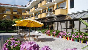 Patio de hotel con mesas al aire libre, sombrillas amarillas y arreglos florales.
