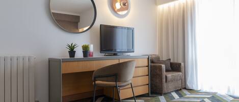A modern hotel room with a desk, chair, television, and a large mirror.