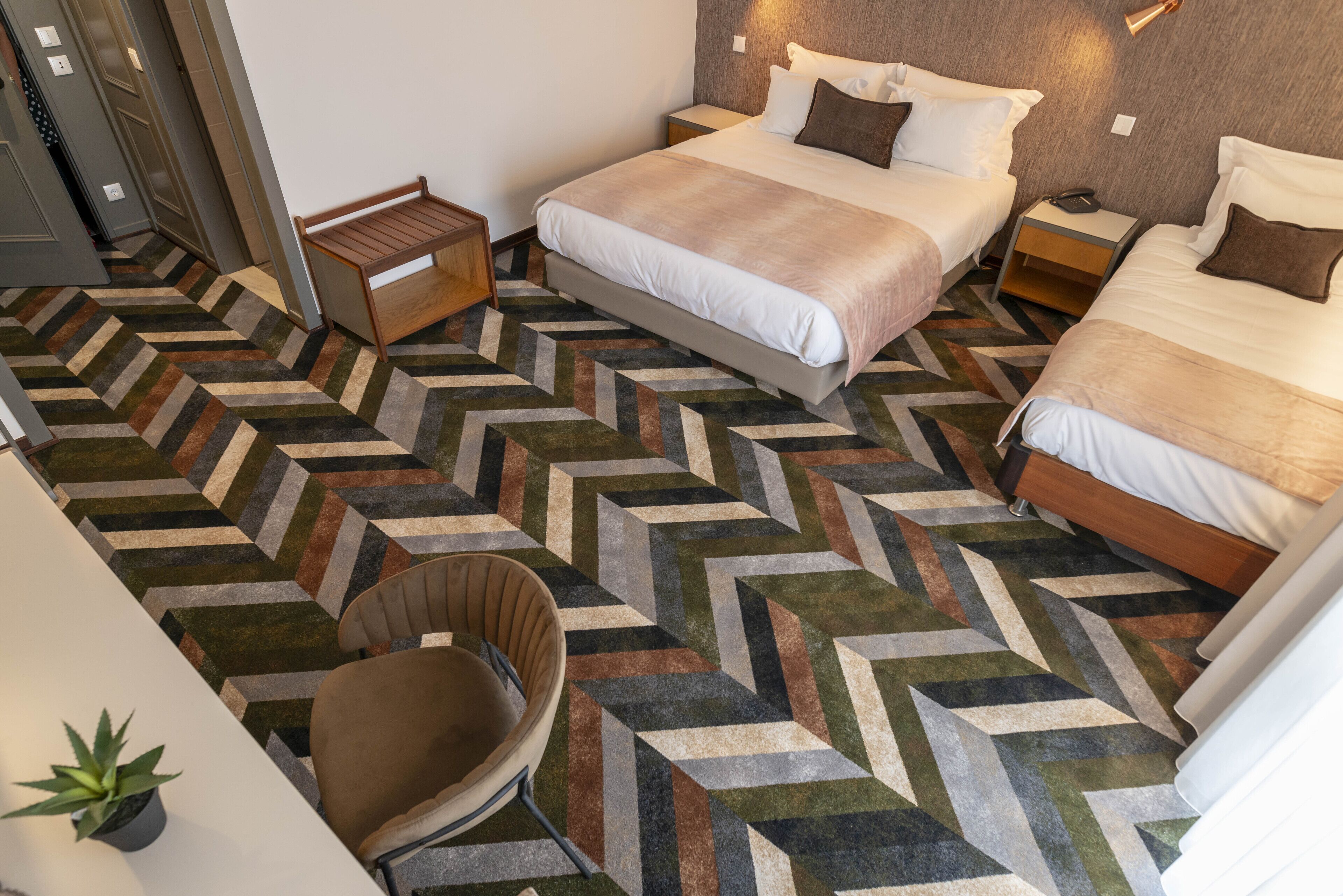 A hotel room with a large bed, two bedside tables, a chair, and a patterned carpet.