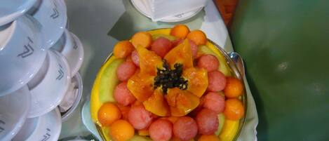A fruit platter on a table with stacked white plates and a spoon.