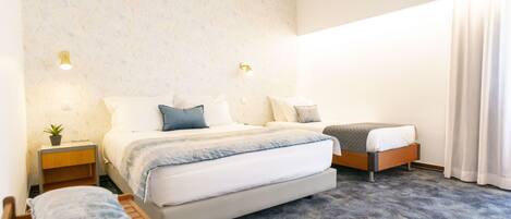 Ein Hotelzimmer mit einem großen Bett, einem kleineren Bett, einem Nachttisch mit Lampe und einem kleinen Tisch mit Kissen.