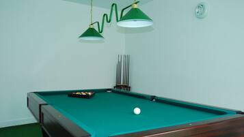Een biljarttafel met een groene viltkleed, twee hanglampen en een set poolkeus.