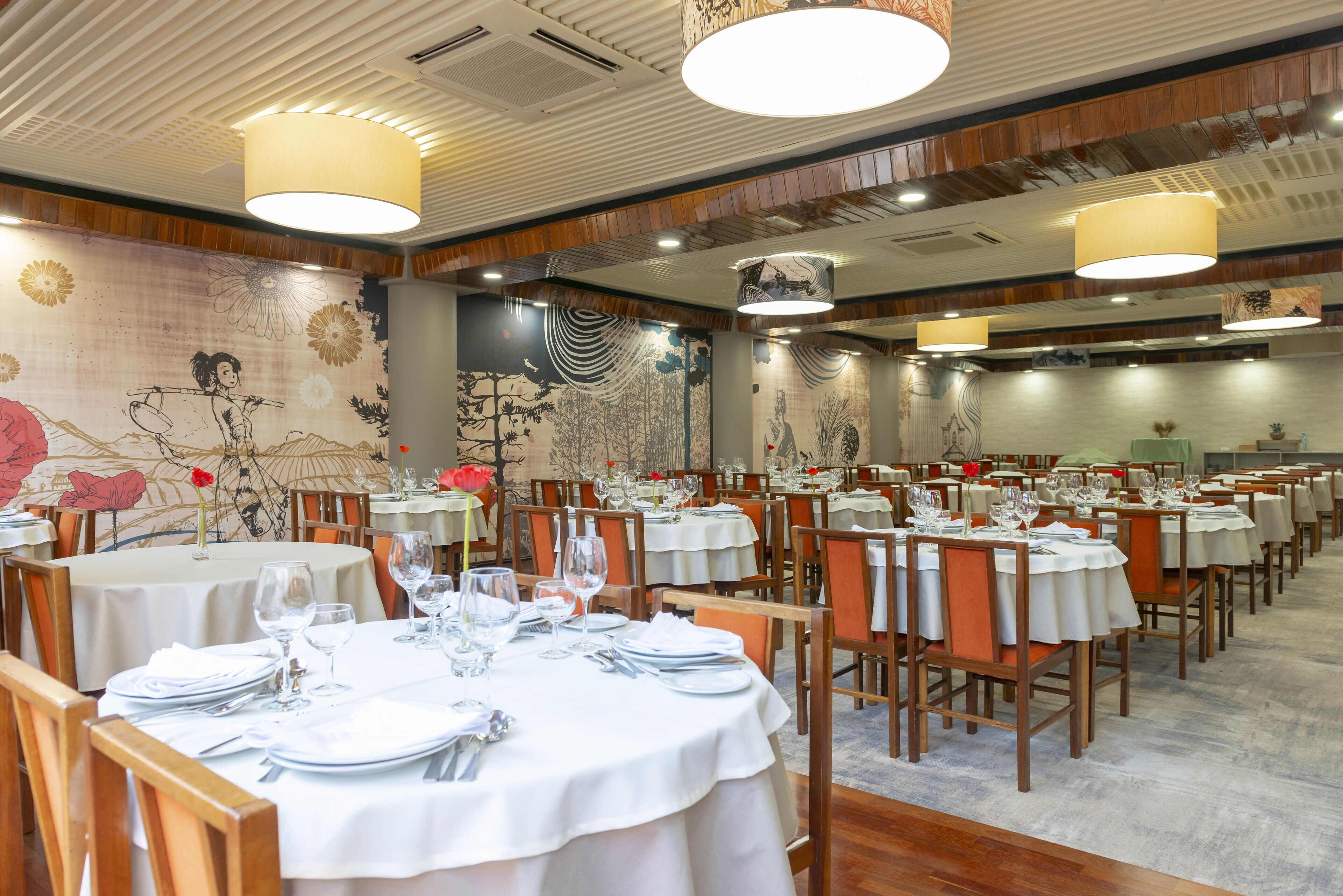 Restaurante com várias mesas redondas, dispostas com toalhas brancas, cadeiras e talheres.