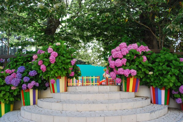 A set of outdoor steps leading to a playground, surrounded by lush greenery and colorful painted fences. - D. Afonso Hotel & SPA (Leiria)