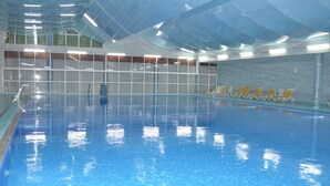 Una piscina interior con agua azul cristalina, suelo de baldosas y sillas de sol amarillas a lo largo del borde.