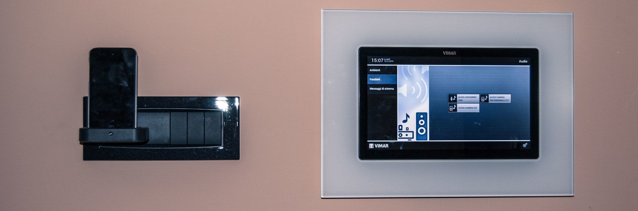 Un dispositivo montado en la pared con una pantalla que muestra una interfaz de usuario, y un teléfono separado también montado en la pared.