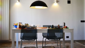A dining area with a white table, two black chairs, a black pendant light, and a wall-mounted light fixture. - B&B La Casa Di Adua (Porto Sant'Elpidio)