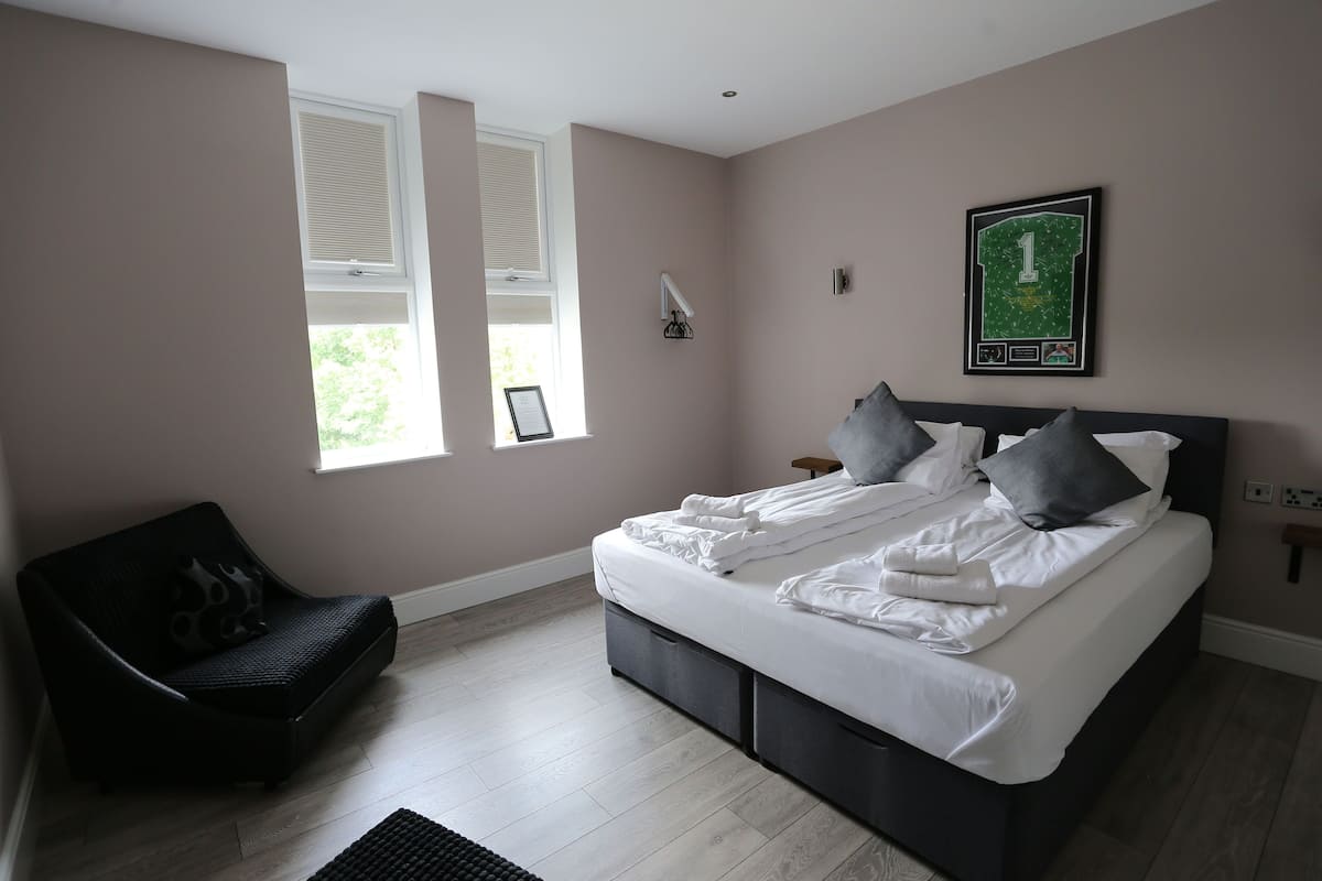 A bedroom with a bed, a chair, a window, and a wall-mounted picture.