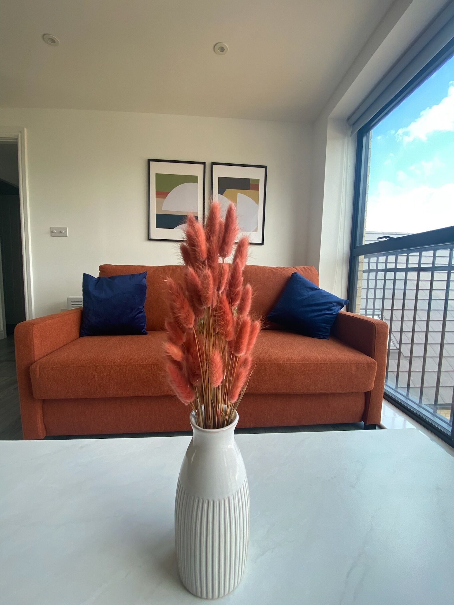 A living room with a sofa, a vase with pampas grass, and two framed pictures on the wall.