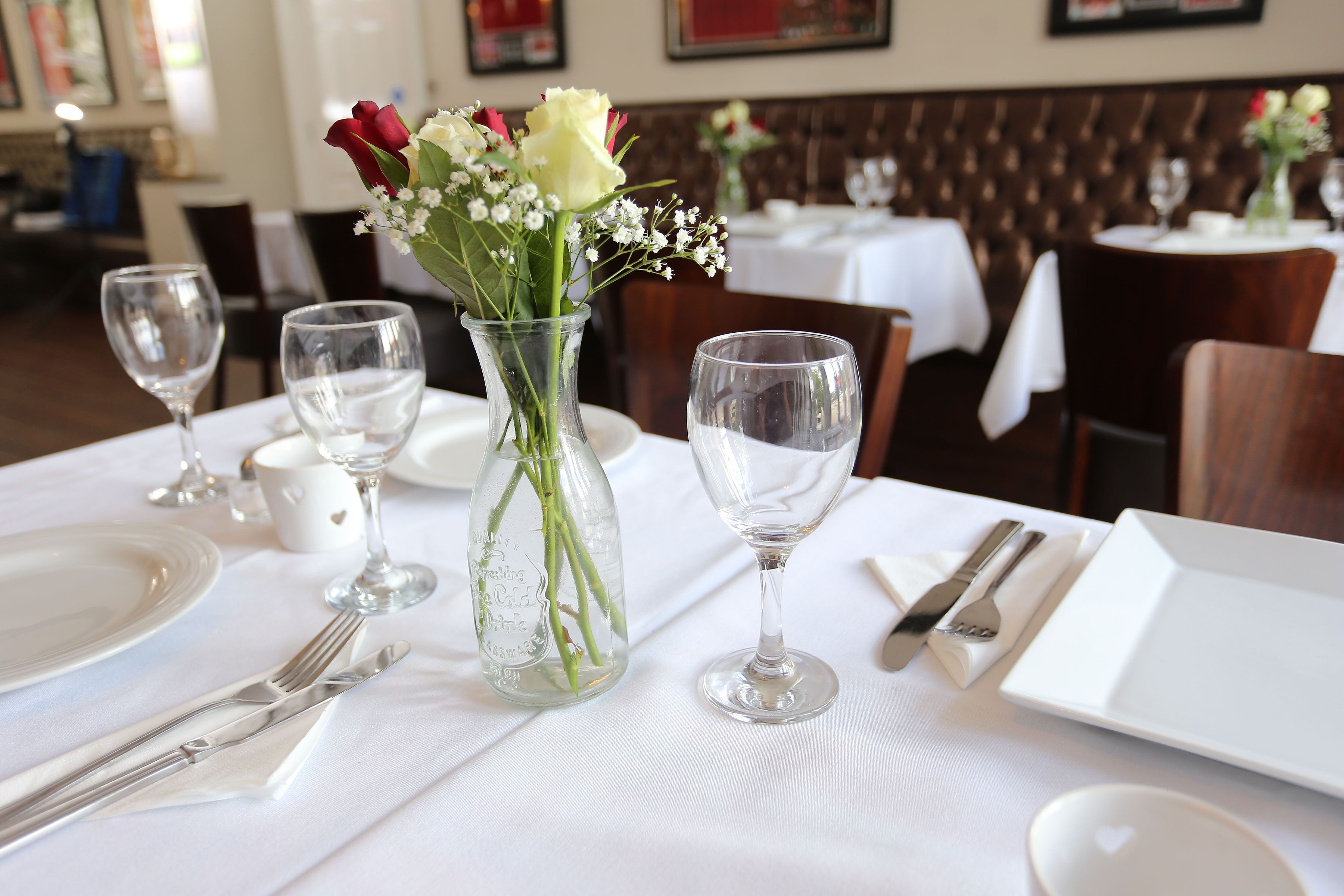 A dining table set with a vase of flowers, wine glasses, and cutlery.