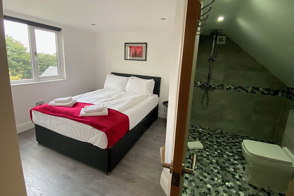 A bedroom with a bed, a shower, and a window.