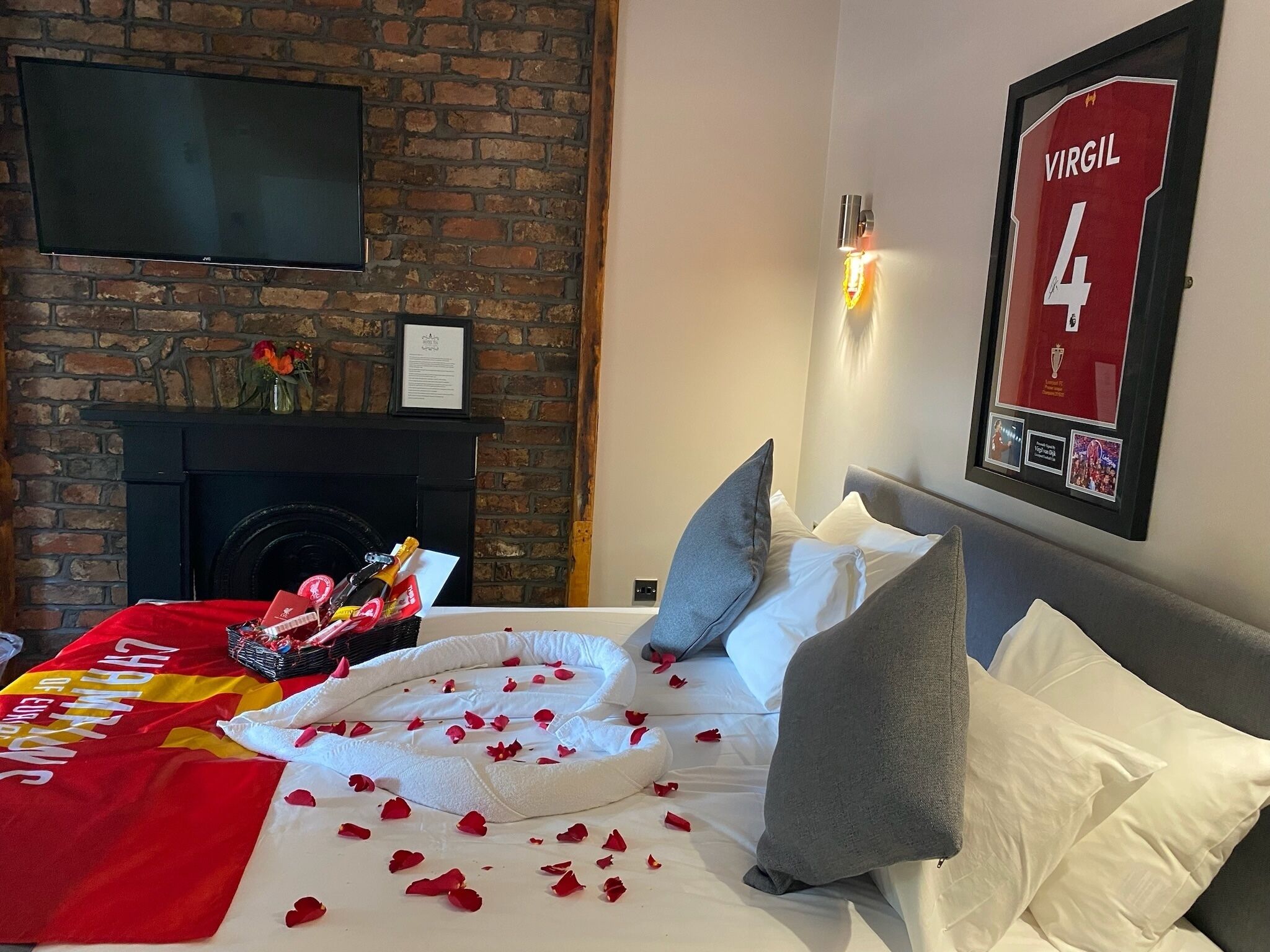Ein Hotelzimmer mit Backsteinwand, einem Flachbildfernseher, einem gerahmten Trikot und einem Bett mit Rosenblättern.