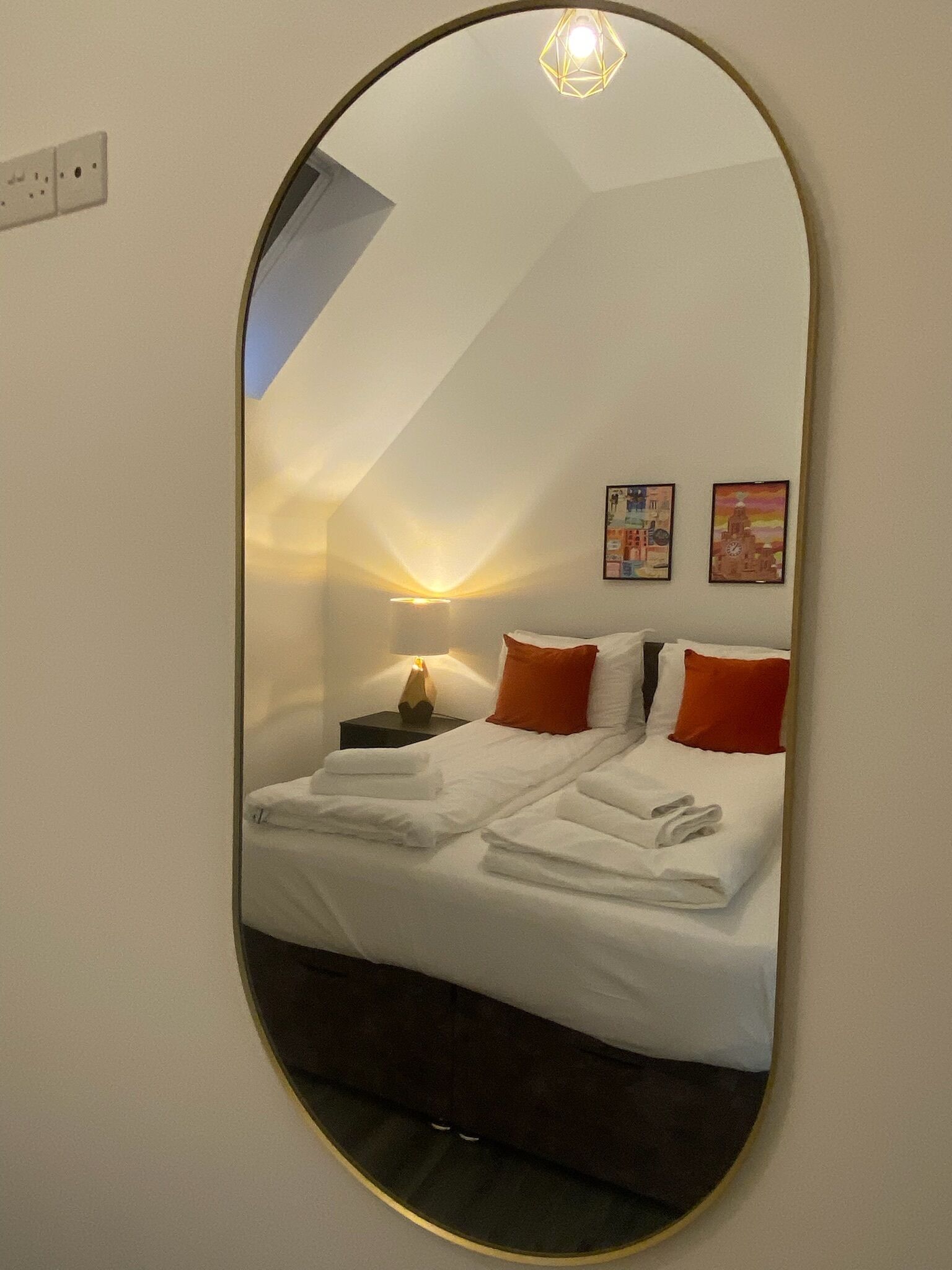 Una camera da letto con un letto, cuscini, un comodino, una lampada e due quadri appesi al muro.
