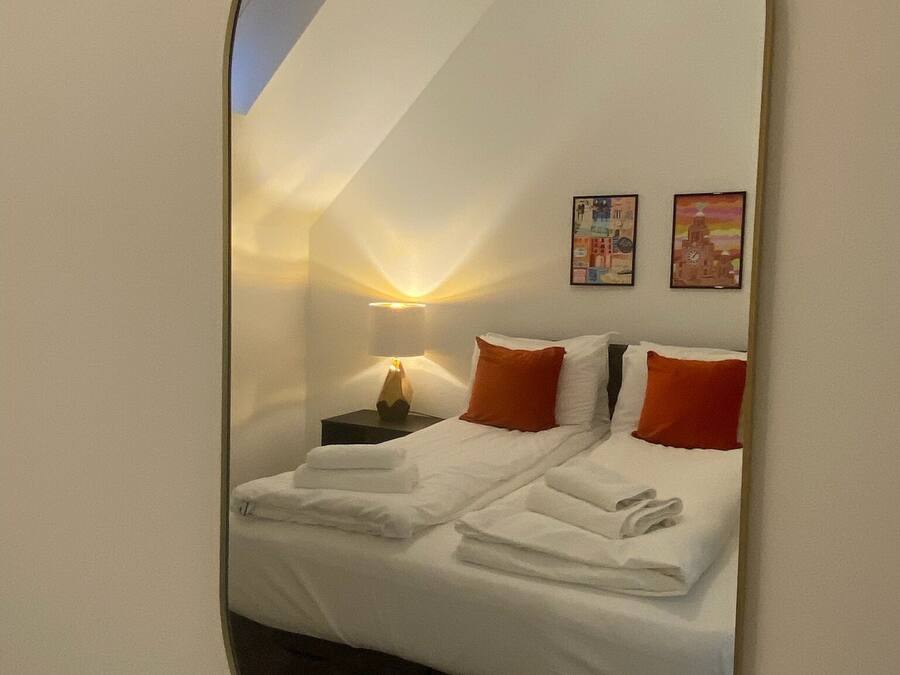 Une chambre à coucher avec un lit, des oreillers, une table de chevet, une lampe et deux tableaux accrochés au mur.