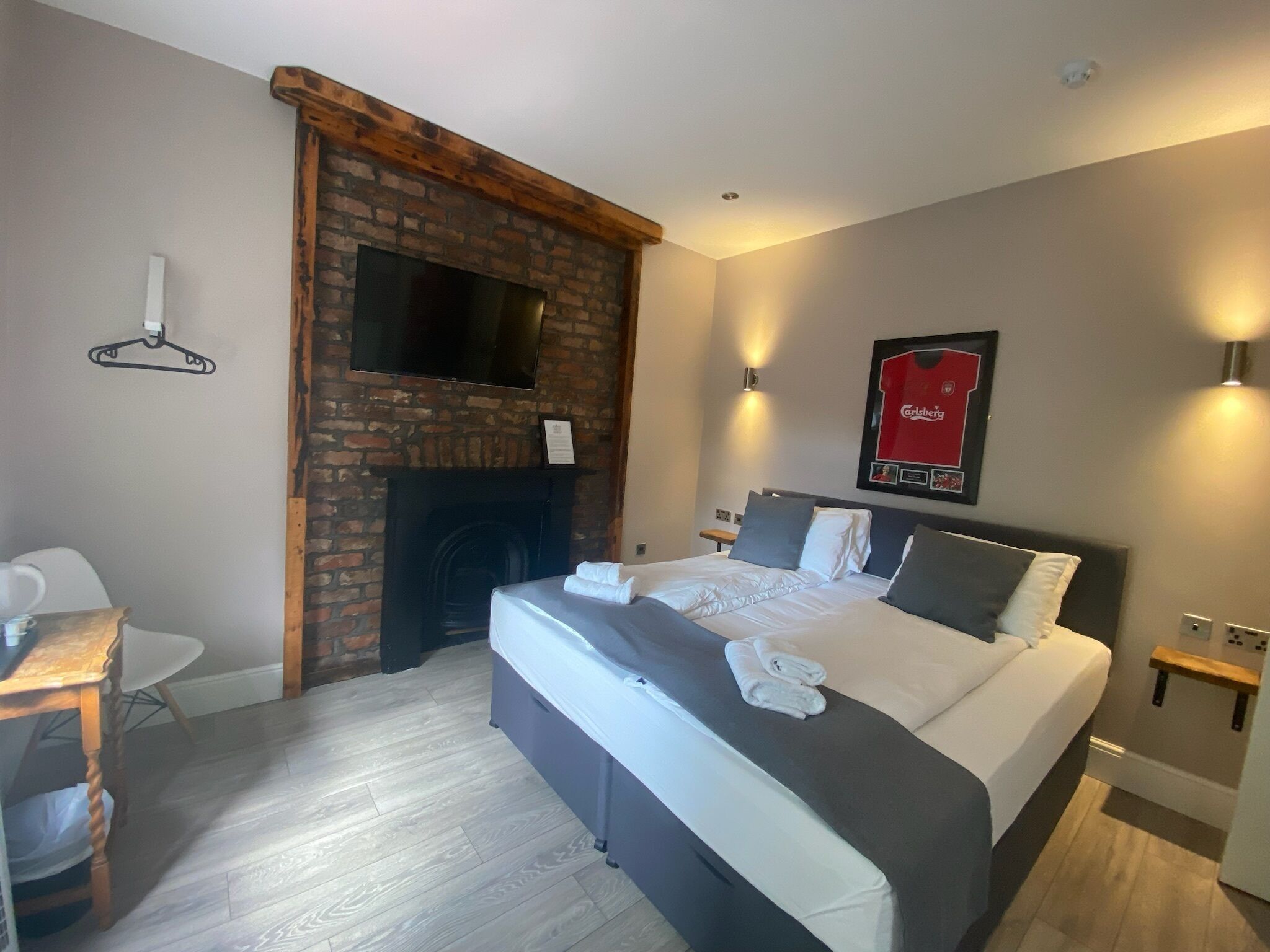 A hotel room with a brick fireplace, a bed with white bedding, a flat-screen TV mounted on the wall, and a framed sports jersey on the wall.