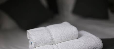 A neatly folded white towel on a dark-colored pillow in a dimly lit room.