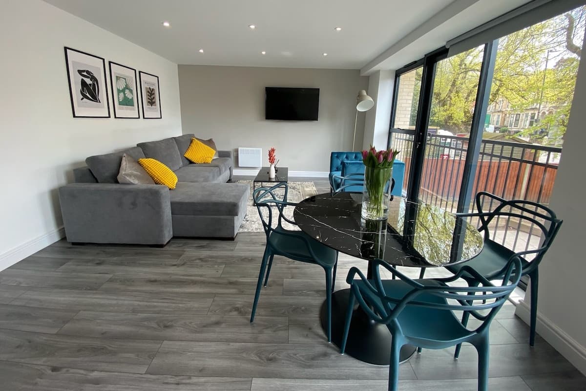 A modern living room with a grey sofa, teal chairs, a black coffee table, and a TV mounted on the wall.