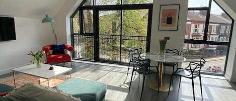 A spacious loft with a high ceiling, large windows, a dining area, and a living room with a sofa and a red chair.